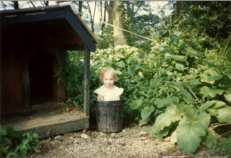 two year old me standing in a dog water bucket in a frilly white dress